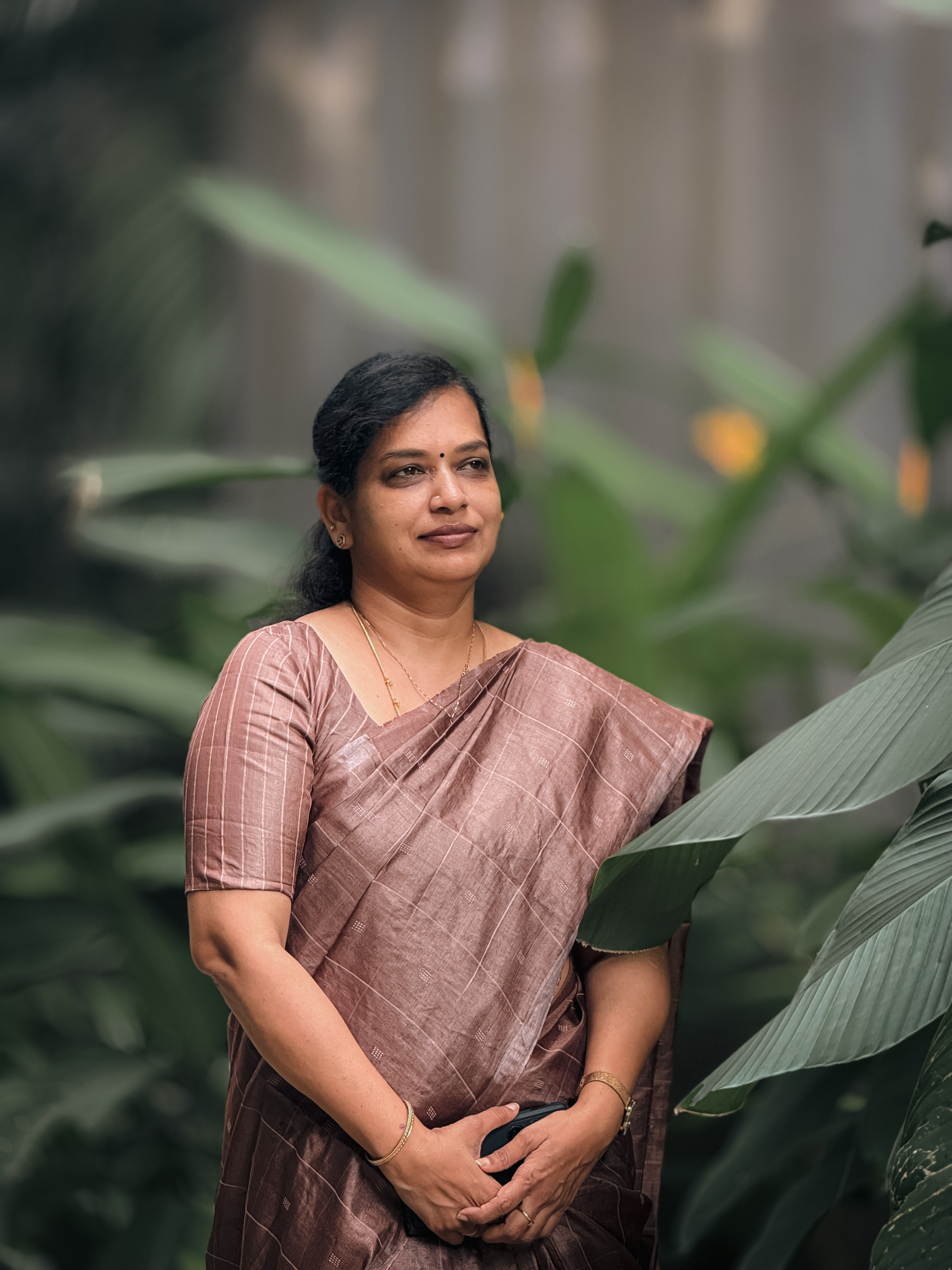 Geetha wearing a mauve sari beside green plants